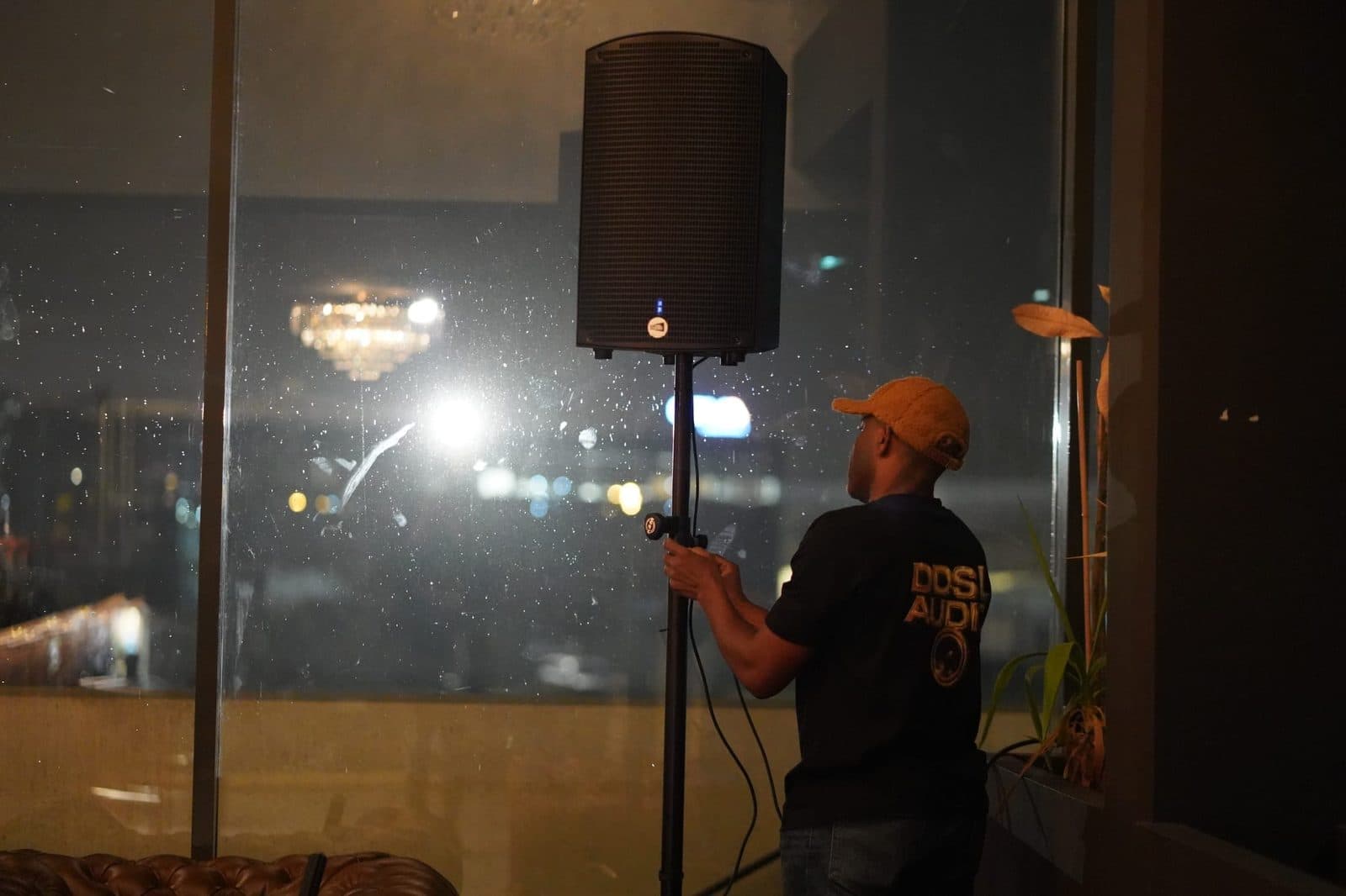Technicien DDSL Audio réglant la hauteur d'une enceinte sur pied dans une salle, de nuit.