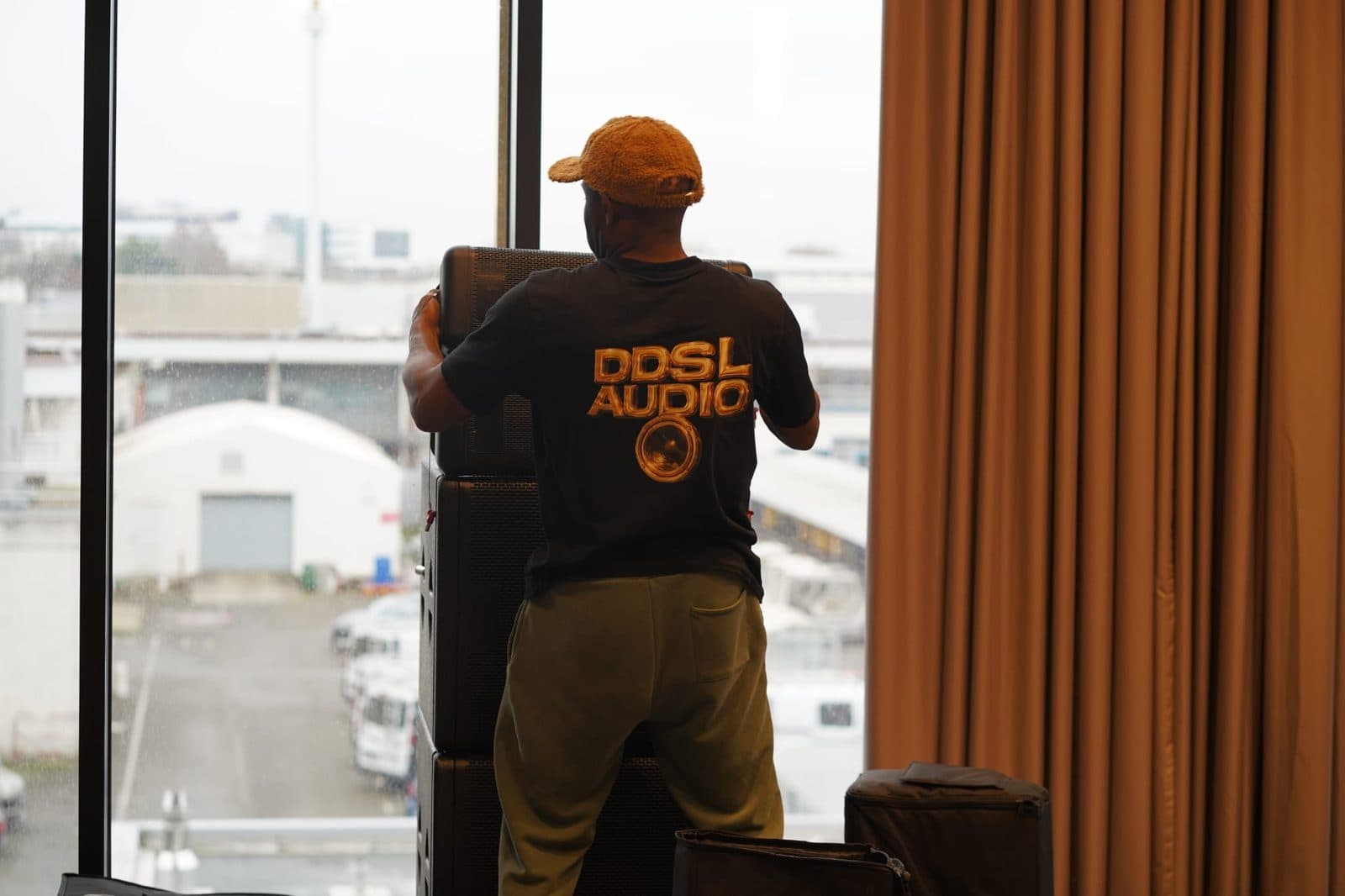 Technicien en t-shirt DDSL Audio positionnant des enceintes empilées devant une baie vitrée.